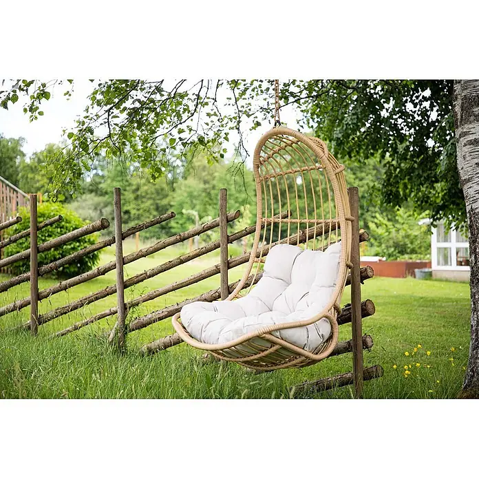 Ebuy24 Hängesessel Pulau - L x B x H: 70 x 77 x 120 cm, Natur - Ein hellbrauner Rattan-Hängesessel mit weichen weißen Kissen, von einem Ast in einem grünen Garten hängend.