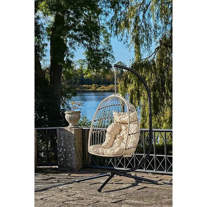 Ebuy24 Hängesessel Petra - Sonstiges, Grau - Ein eiförmiger Hängesessel mit beigem Kissen auf schwarzem Metallgestell auf einer Außenterrasse.