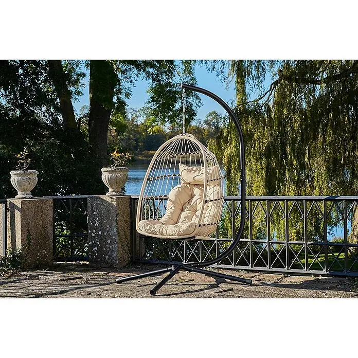 Ebuy24 Hängesessel Petra - Sonstiges, Grau - Beiger geflochtener Hängesessel mit cremefarbenem Kissen auf schwarzem Gestell, auf einer Terrasse am Wasser.