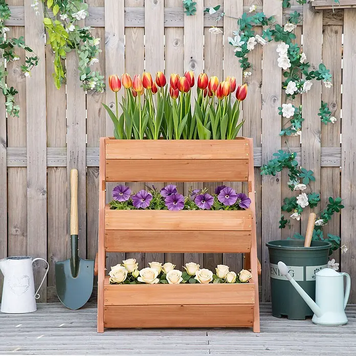 Outsunny Hochbeet - Holz, Braun - Ein dreistufiger hellbrauner Holzpflanzkasten mit bunten Blumen, darunter rot-gelbe Tulpen, lila Petunien und cremefarbene Rosen.