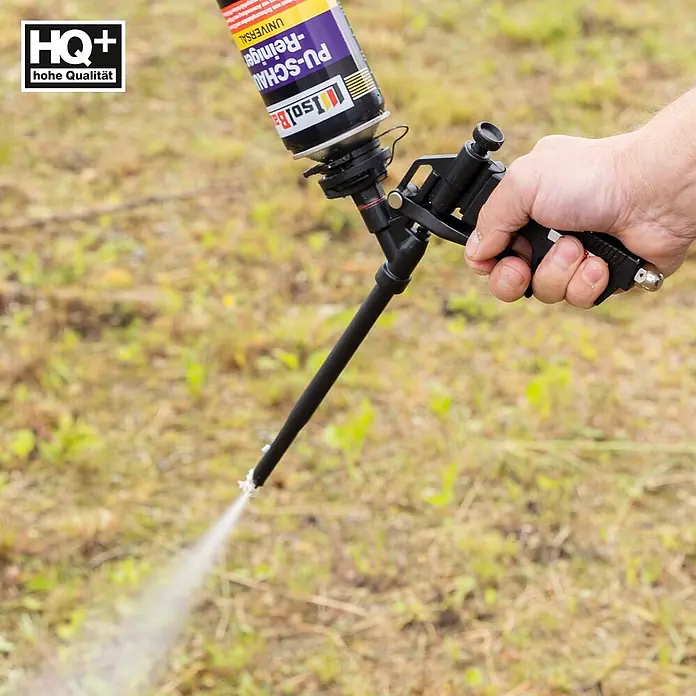 IsolBau Bauschaum PU-Schaum-Reiniger 1 x 500 ml - 500 ml - Eine Hand hält eine schwarze PU-Schaumpistole mit Reinigerdose und sprüht Schaum im Freien.