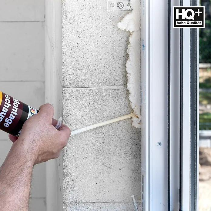 IsolBau Adapterschaum Montageschaum mit Aussprührohr 24 x 750 ml - 750 ml - Eine Hand trägt weißen Montageschaum mit einem Strohhalm aus einer Dose auf, um einen Fensterrahmen an einer Mauer abzudichten.