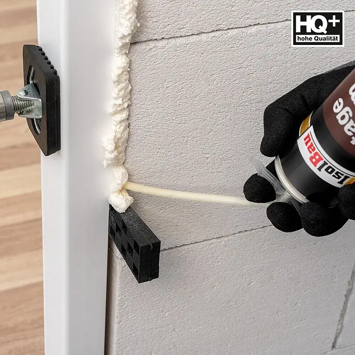 IsolBau Adapterschaum Montageschaum mit Aussprührohr 1 x 750 ml - 750 ml - Eine behandschuhte Hand trägt weißen isolBau Montageschaum auf, um den Spalt zwischen weißem Türrahmen und hellgrauer Wand abzudichten.