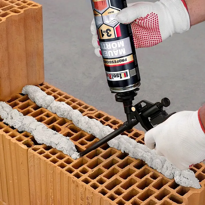 IsolBau Klebeschaum PU Mauermörtel - 6 x 750ml, PU-Reiniger - 500 ml, Schaumpistole - 750 ml - Eine Hand trägt grauen Schaummörtel aus einer IsoLBau Dose mit einer Auftragspistole auf Hohlziegel auf.