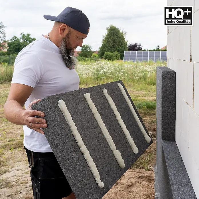 IsolBau Klebeschaum Profi Dämmstoffkleber 3 x 750 ml - 750 ml - Mann bringt eine dunkelgraue Dämmplatte mit weißen Klebestreifen an einer weißen Wand an.