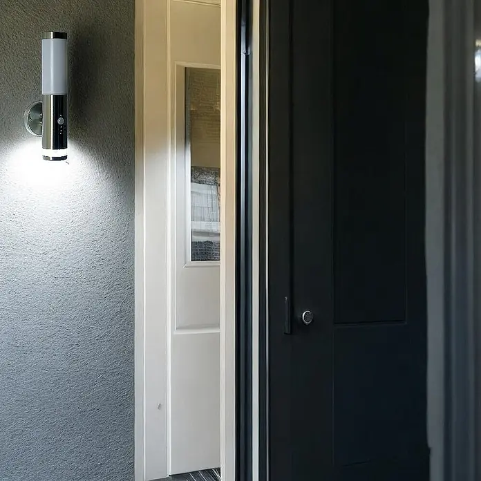 DAPO Außenwandleuchte Lisa, mit LED-Kranz, Edelstahl, E27, IP44 -  - Silber-weiß zylindrische Außenleuchte mit Sensor, die eine Wand neben einer offenen Tür beleuchtet.