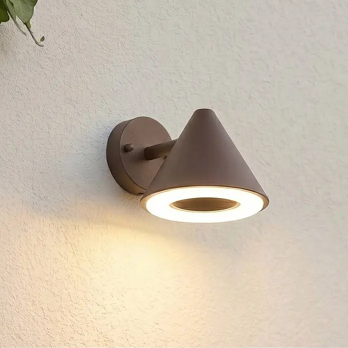 Lindby Außenwandleuchte Soran - braun / rost, braun / rost, IP44 - Dunkelbraune konische Außenwandleuchte mit beleuchtetem LED-Ring, an einer strukturierten Wand montiert.