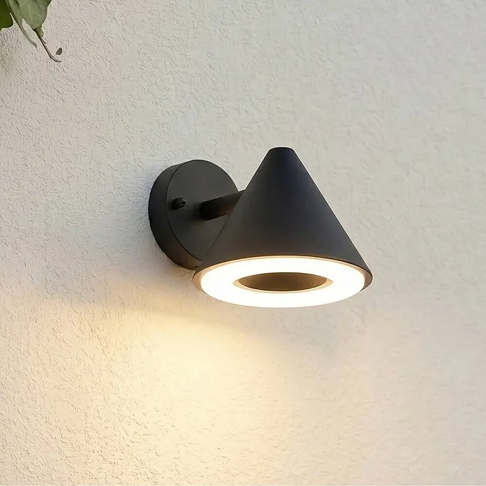 Lindby Außenwandleuchte Soran - schwarz, schwarz, IP44 - Mattschwarze konische Wandleuchte mit beleuchtetem Ring, an einer strukturierten Wand montiert, warmes Licht abgebend.