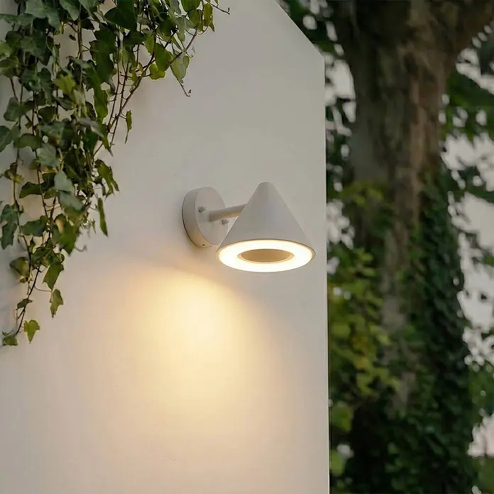 Lindby Außenwandleuchte Soran - alu / grau / zink, alu / grau / zink, IP44 - Weiße konische Außenwandleuchte, an einer Wand montiert, die warmes Licht nach unten strahlt.