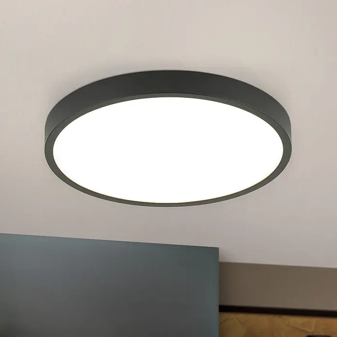 Orion Leuchten LED-Panel rund -  - Ein dunkelgraues, rundes Deckenlicht ist bündig an einer weißen Decke montiert und strahlt helles weißes Licht aus.