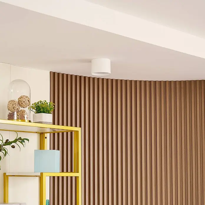 Lindby Deckenstrahler Nivoria - weiß / opal - Weiße zylindrische Deckenleuchte in einem modernen Raum mit Holzlamellenwand.
