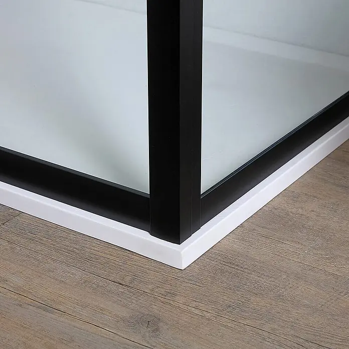 Kiamami Valentina Eckdusche - 100 x 70 x 190 cm, Farblos, Schwarz, Stärke: 6 mm - Ecke einer modernen Duschkabine mit weißem Sockel, schwarzem Rahmen und klaren Glasplatten auf Holzboden.