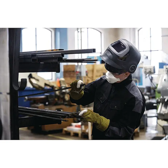 3M Schweißhelm Speedglas G5-03 E -  - Arbeiter mit Schutzausrüstung handhabt dunkle, rechteckige Metallstangen in einem Lagerregal.