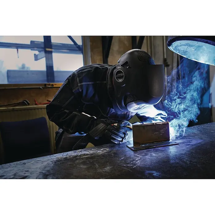 3M Schweißhelm Speedglas G5-03 E -  - Schweißer mit schwarzem Helm und Handschuhen bearbeitet ein Metallstück, heller Schweißlichtbogen sichtbar.