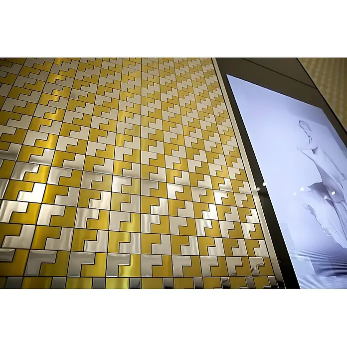 ALLOY Mosaikfliese Mosaik Fliese massiv Edelstahl hochglänzend grau 1,6mm stark Kink-S-S-M - 307 x 304 mm, Grau, Silber, Hochglänzend - Wand mit metallischen gold- & silberfarbenen L-förmigen Fliesen in geometrischem Muster, neben einem Bildschirm.
