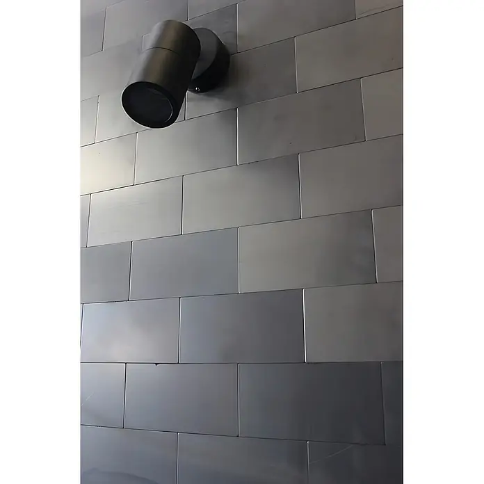 ALLOY Mosaikfliese Mosaik Fliese massiv Metall Rohstahl gewalzt grau 1,6mm stark Subway-RS - 76 x 152 mm, Grau, Sonstiges - Schwarzer zylindrischer Strahler an einer Wand aus rechteckigen Metallpaneelen montiert.