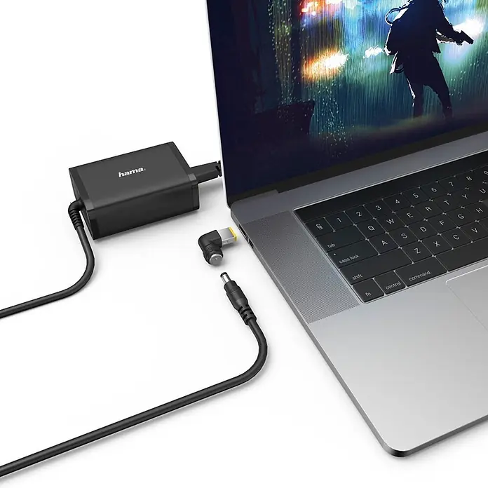 Hama Ladegerät 00200002 15-19V/65W - Schwarz, L x B x H: 3,1 x 5,5 x 1,2 cm - Schwarzes Hama Laptop-Netzteil lädt einen Laptop, mit einem austauschbaren Stecker daneben.