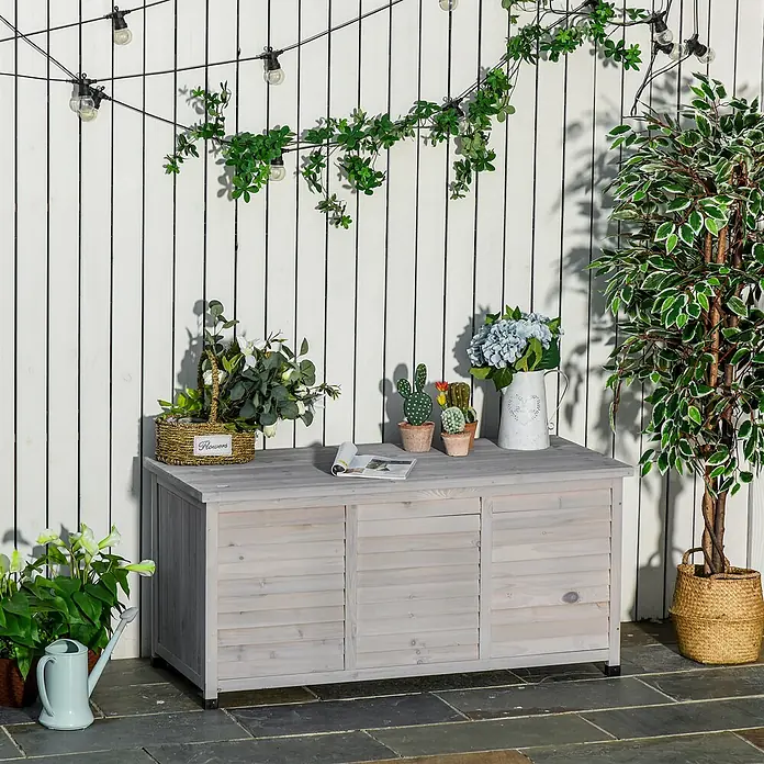 Outsunny Garten-Aufbewahrungsbox - Hellgrau, Holz - Helle graue Holz-Gartenaufbewahrungsbank mit drei Lamellenfächern, als Ablagefläche für Pflanzen und Dekoration auf einer Terrasse genutzt.