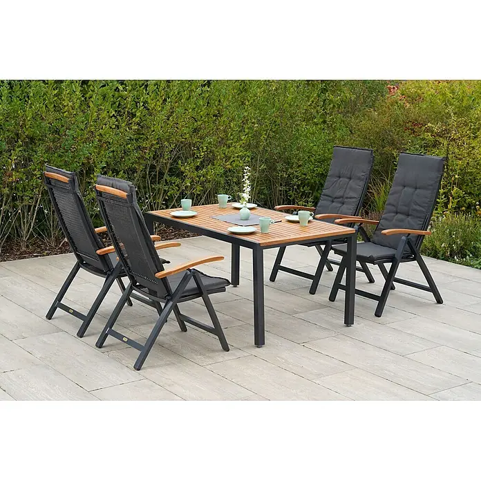 Merxx Gartentisch-Set Tilos - Gesamtumfang: 9 -tlg., Aluminium/Akazie, Klappbar - Gartenessgruppe mit Holztischplatte, dunklem Gestell und vier Stühlen mit dunkelgrauem Netzgewebe und Auflagen, Holzarmlehnen, auf einer Terrasse.