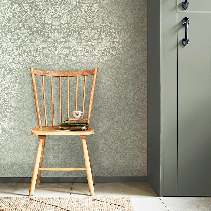 William Morris At Home Vliestapete Vliestapete Erdbeerdieb - Grün, Floral, 10 x 0,52 m - Salbeigrüner Tapete mit floralem und Vogelmotiv an einer Wand in einem Raum installiert.