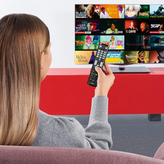 Hama Universal-Fernbedienung für Samsung TVs - Schwarz - Person hält eine schwarze Fernbedienung und zeigt sie auf einen Fernseher mit einer Streaming-Oberfläche.