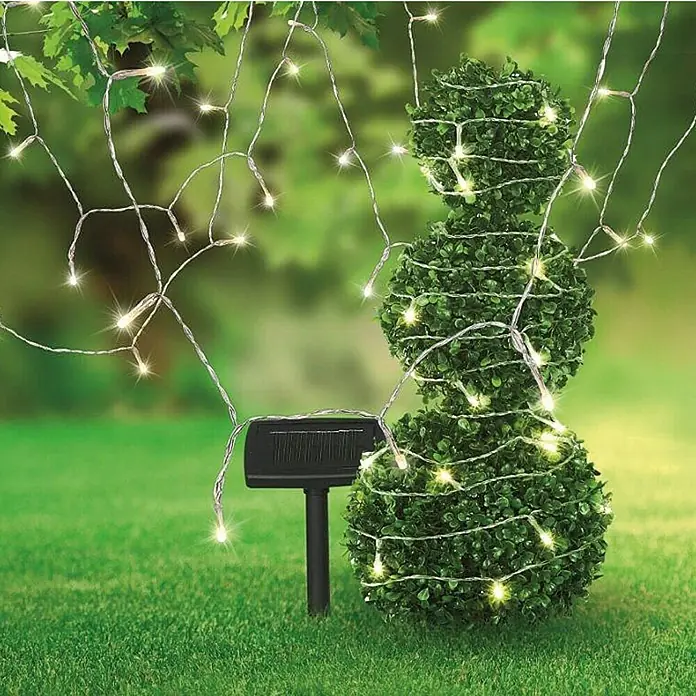 Globo Solar-Lichterkette - 20 m, IP44, Lichtfarbe: Warmweiß - Dekorative Solar-Lichterkette, um einen Buchsbaum gewickelt, mit einem Solarpanel auf einem grünen Rasen für den Außenbereich.