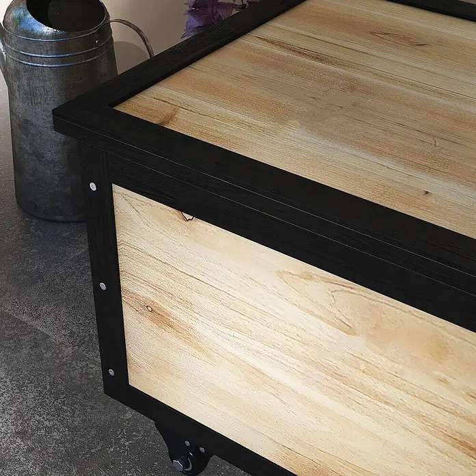 Outsunny Garten-Aufbewahrungsbox - Naturholz - Nahaufnahme einer rustikalen Holztruhe mit hellen Holzplatten und schwarzem Rahmen, auf Rollen, auf einem Betonboden.