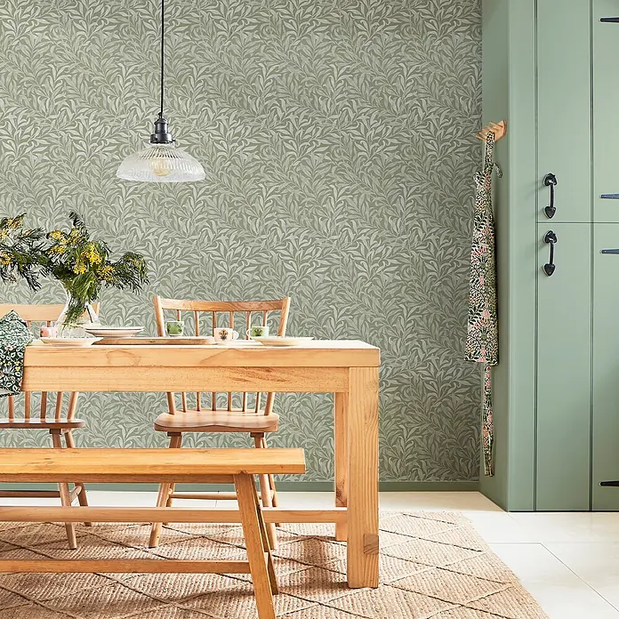 William Morris At Home Vliestapete Vliestapete Weidenzweig - Salbeigrün, Sonstiges, 10 x 0,52 m - Sanfte olivgrüne Tapete mit zartem weißem Weidenblattmuster ziert eine Esszimmerwand mit Holzmöbeln.
