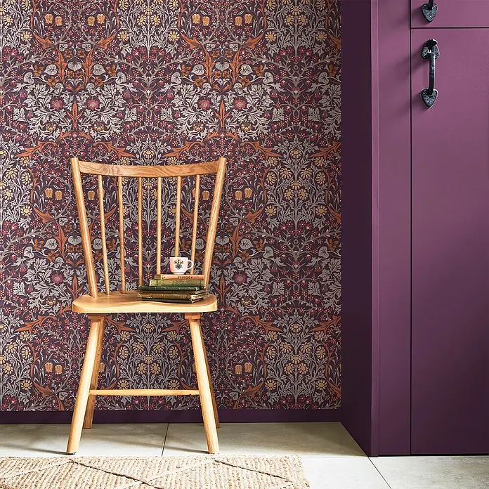 William Morris At Home Vliestapete Vliestapete Schlehdorn - Lila, Floral - Florale Tapete in Dunkellila mit orangefarbenen und grauen botanischen Mustern, die eine gemütliche Ecke schmückt.