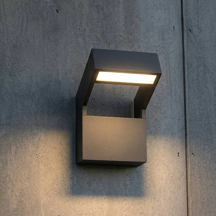 Arcchio Außenwandleuchte Kovato - alu / grau / zink, IP65 - Eine moderne dunkelgraue Außenwandleuchte an einer Betonwand, die warmes Licht nach unten wirft.