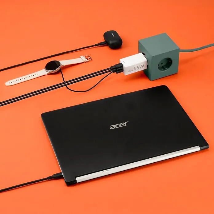 Hama Schnellladegerät 00201996 GaN 2x USB-C 1x USB-A Mini PD 65 W - Weiß - Weißes GaN 65W Ladegerät in grüner Würfel-Steckdosenleiste, lädt schwarzen Laptop, weiße Smartwatch und schwarze Ohrhörer.