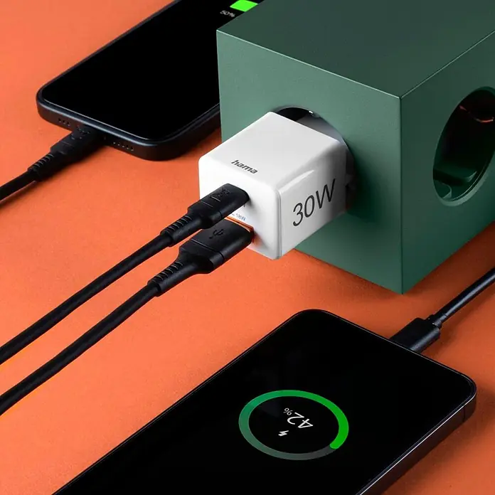 Hama Schnellladegerät 00201992 1x USB-C 1x USB-A Mini PD 30 W - Weiß - Weißes Hama 30W Dual-Port Ladegerät in grüner Steckdose, lädt zwei schwarze Smartphones mit schwarzen Kabeln.