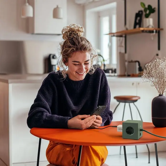 Hama Schnellladegerät 00201992 1x USB-C 1x USB-A Mini PD 30 W - Weiß - Grüner Stromwürfel mit einer Steckdose und zwei USB-Anschlüssen, lädt ein Smartphone auf einem orangefarbenen Tisch.