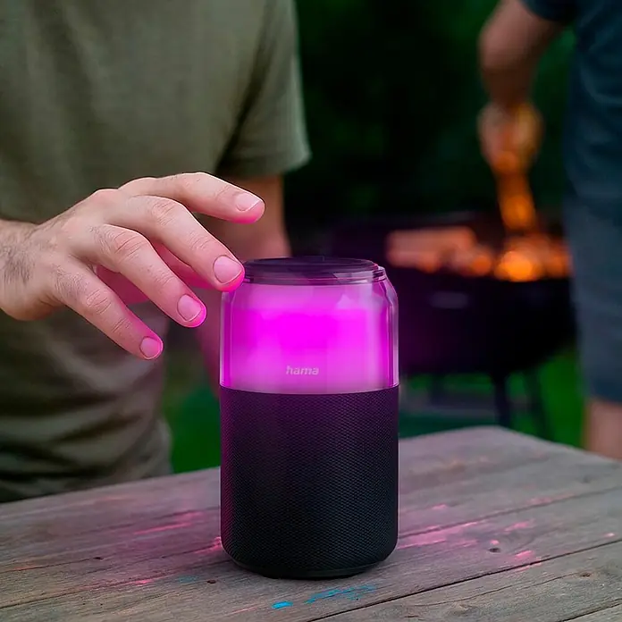 Hama Bluetooth-Lautsprecher "Can Speaker" - Schwarz - Schwarzer Lautsprecher mit leuchtend pinker Oberseite auf Holztisch, Hand interagiert bei Outdoor-Treffen.