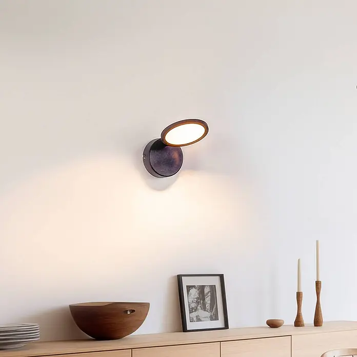 Lindby Deckenstrahler Manel - schwarz, schwarz - Dunkelbraune Wandleuchte mit drehbarer Scheibe, strahlt warmes Licht aus, montiert über einem Holzsideboard.