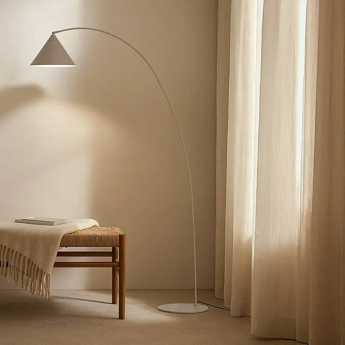 Lindby Stehleuchte Triangolo - Höhe: 195 cm, creme / amber, creme / amber, E27 - Eine minimalistische Bogenstehlampe mit konischem Schirm beleuchtet eine gemütliche Zimmerecke mit Holzbank und Vorhängen.