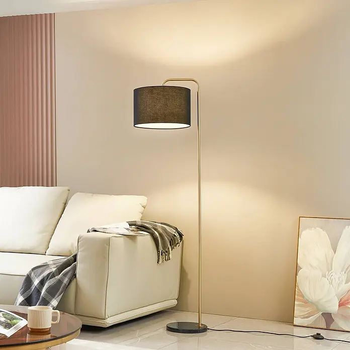 Lindby Stehleuchte Hillary - Höhe: 153 cm, messing / gold, schwarz, E27 - Goldene Stehlampe mit schwarzem Trommelschirm beleuchtet ein modernes Wohnzimmer.