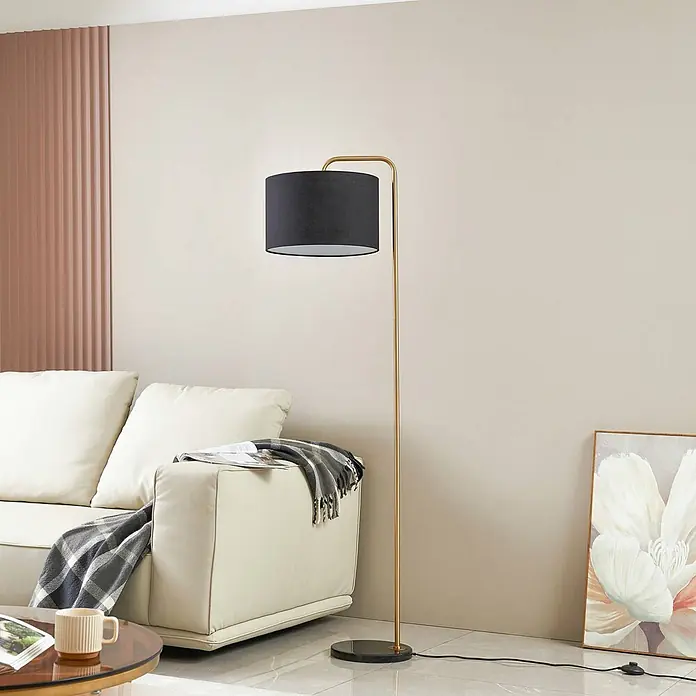 Lindby Stehleuchte Hillary - Höhe: 153 cm, messing / gold, schwarz, E27 - Goldfarbene Stehlampe mit schwarzem zylindrischem Schirm, neben einem weißen Sofa in einem modernen Wohnzimmer.