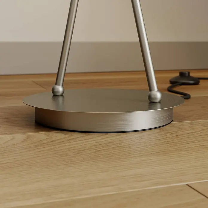 Lucande Stehleuchte Juljana - alu / grau / zink, creme / amber, E14 - Gebürstete Metallbasis einer Stehlampe mit zwei silbernen Beinen auf Holzfußboden neben einem schwarzen Fußschalter.