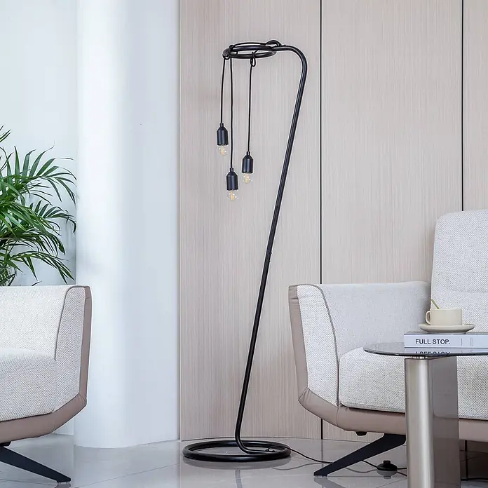 Lindby Stehleuchte Elira - Höhe: 150 cm, schwarz, schwarz, E27 - Große schwarze Metall-Stehlampe mit einzigartigem Bogen-Design und drei hängenden Edison-Birnen, neben einem hellen Sessel.