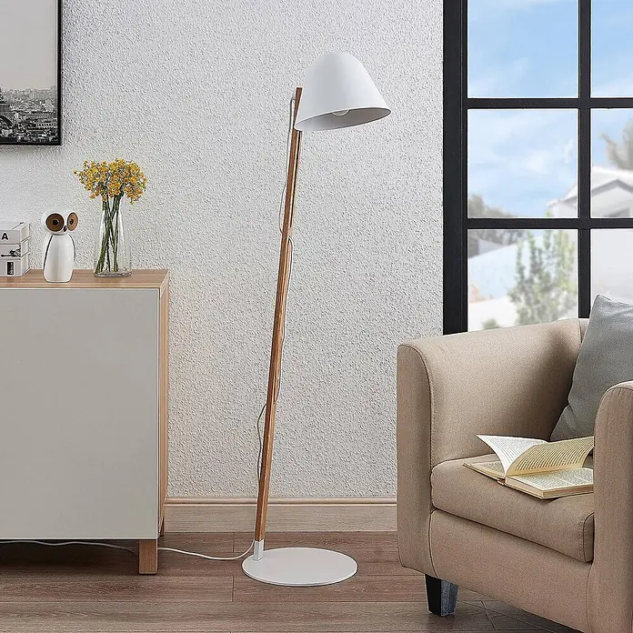 Lindby Stehleuchte Tetja - Höhe: 128 cm, Holz hell, weiß / opal, E27 - Moderne Stehlampe mit weißem konischem Schirm, natürlichem Holzständer und rundem weißem Fuß, die einen Wohnraum beleuchtet.