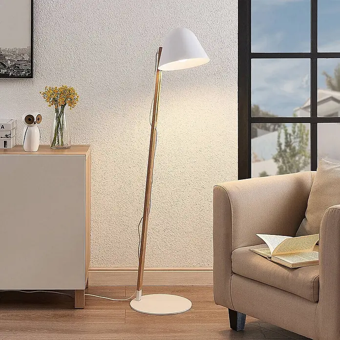 Lindby Stehleuchte Tetja - Höhe: 128 cm, Holz hell, weiß / opal, E27 - Moderne Stehlampe mit weißem Kegelschirm, Holzständer und rundem weißem Fuß, beleuchtet ein gemütliches Wohnzimmer.