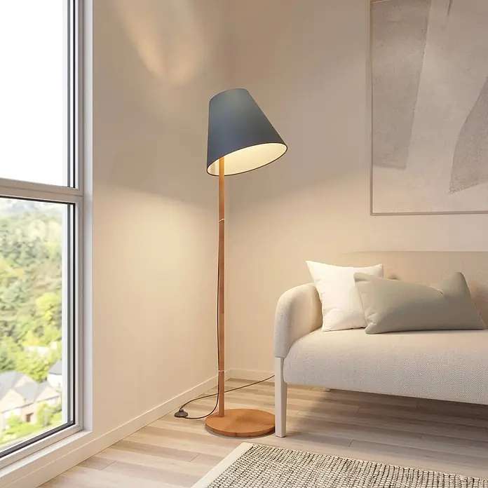 Lucande Stehleuchte Jinda - Holz dunkel, blau, E27 - Stehlampe aus Holz mit dunklem Schirm, spendet warmes Licht in einem Wohnzimmer neben einem Sofa.