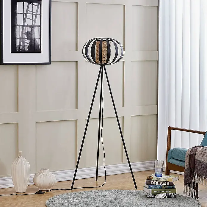 Lindby Stehleuchte Tamira - Höhe: 143 cm, schwarz, schwarz, E27 - Schwarze Metall-Dreibein-Stehlampe mit natürlichem Rattanschirm, steht in einem modernen Wohnzimmer.