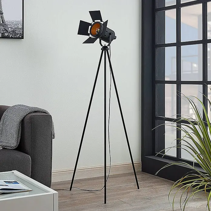 Lindby Stehleuchte Devon - Höhe: 140 cm, schwarz, schwarz, E27 - Hohe schwarze Stativ-Stehleuchte mit Klappen und orangefarbener Glühbirne, im Wohnzimmer neben einem grauen Sofa.