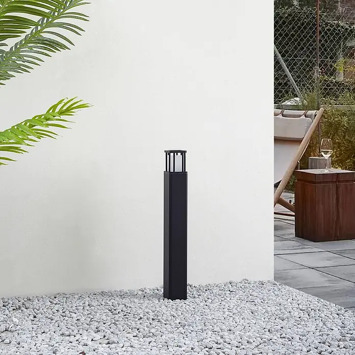 Lucande Außenlaterne Dakil -  - Schwarze rechteckige Außenleuchte auf weißen Kieselsteinen, die einen Terrassenbereich beleuchtet.