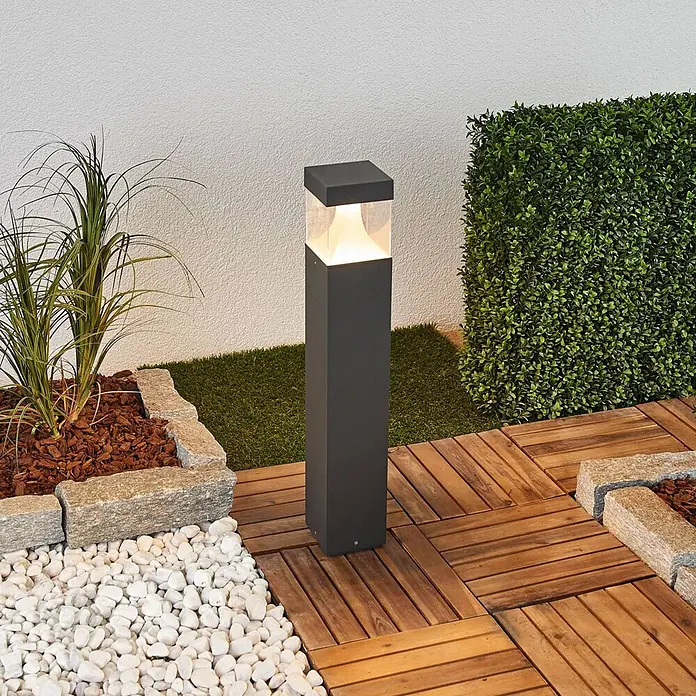 Lucande Außenlaterne Egon -  - Dunkelgraue quadratische Außenleuchte erhellt einen Gartenweg, umgeben von Terrassendielen und Pflanzen.