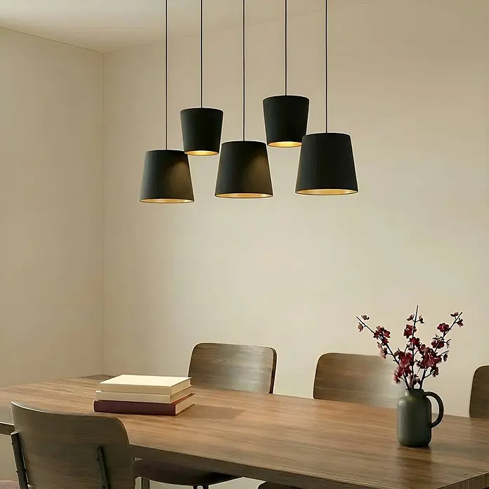 Lucande Pendelleuchte Thamila - schwarz, Schwarz, gold, messing, E27 - Fünf schwarze Pendelleuchten mit goldener Innenseite beleuchten einen Holztisch.