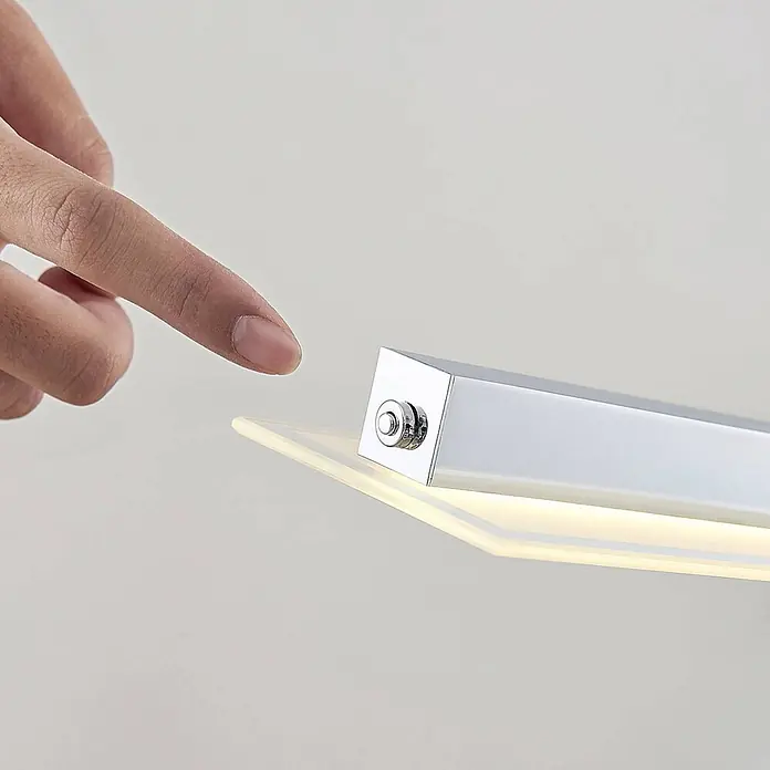 Lindby Pendelleuchte Sladja - L x B x H: 100 x 10 x 4 cm, chrom, satiniert, klar - Finger berührt Knopf an beleuchteter Chrom-Leuchte mit durchscheinender Platte.