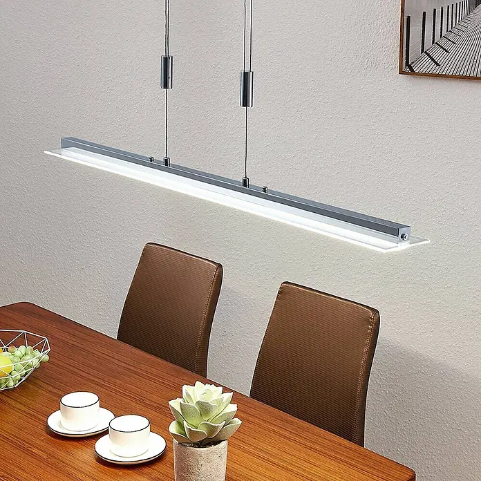 Lindby Pendelleuchte Sladja - L x B x H: 100 x 10 x 4 cm, chrom, satiniert, klar - Eine schlanke, silberne LED-Hängeleuchte strahlt hell über einem Holztisch.